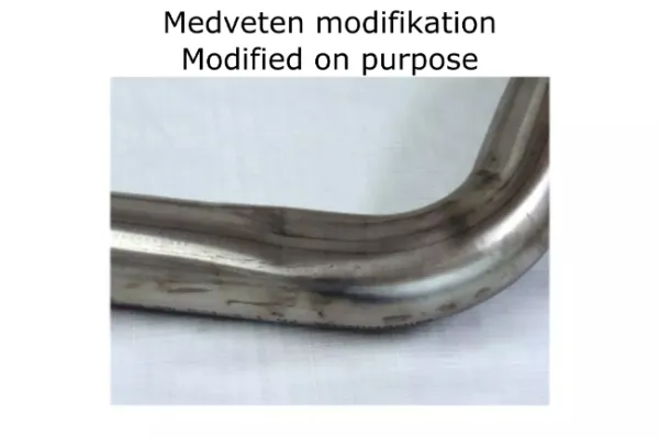 Close-up of a bent stainless steel pipe for a Simons sports exhaust system. The pipe is shiny silver and shows slight signs of wear. "Medveten modification Modified on purpose" is written above the pipe. It is a component for BMW F30 320i, 328i.
