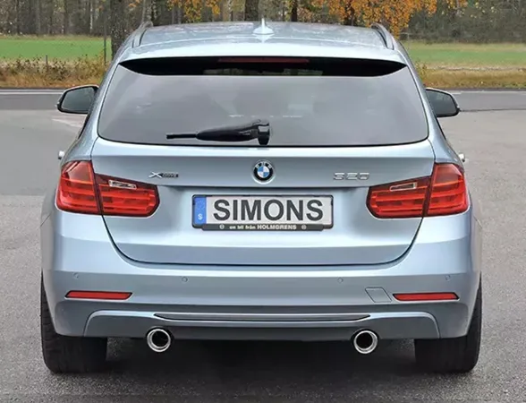 Rear view of a light blue BMW F31 320i estate with duplex sports exhaust system. License plate with Simons lettering. The tailpipes of the exhaust system are arranged on the right and left. Rear lights and BMW logo are visible.