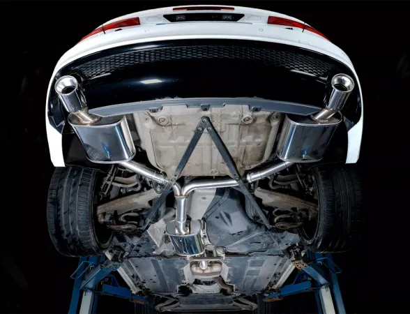 View from below of a white Audi A4 on a lifting platform, showing a Simons stainless steel sports exhaust Duplex L+R with 1x100 mm tailpipes. The picture emphasizes the exhaust system, including pipes and rear silencer.