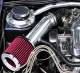 A red, open-style sport air filter in the engine compartment, connected to the engine block via a shiny silver cold-air intake tube. Surrounded by silver engine components, black hoses, and braided lines, the filter really stands out.