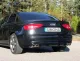 Rear view of a black Audi A4 with duplex sports exhaust system from Simons. You can see the four tailpipes of the exhaust system, the license plate with the lettering "Simons" and the taillights. The car is parked on a road in front of trees.